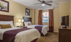 Une chambre d’hôtel avec deux lits, un ventilateur de plafond, une télévision et une fenêtre avec des rideaux.