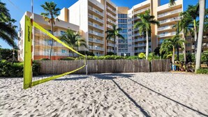Una cancha de voleibol de playa con red, palmeras y un hotel de varios pisos al fondo.