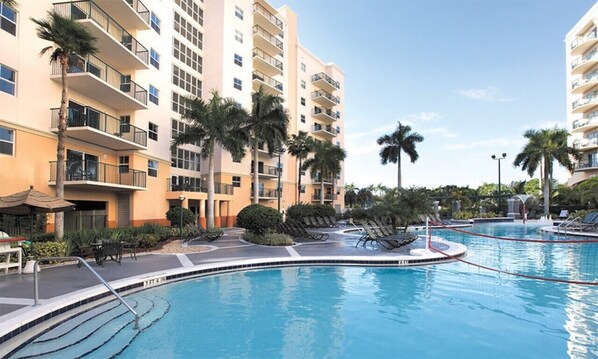 Un hôtel à plusieurs étages, doté de piscines extérieures et bordé de palmiers.