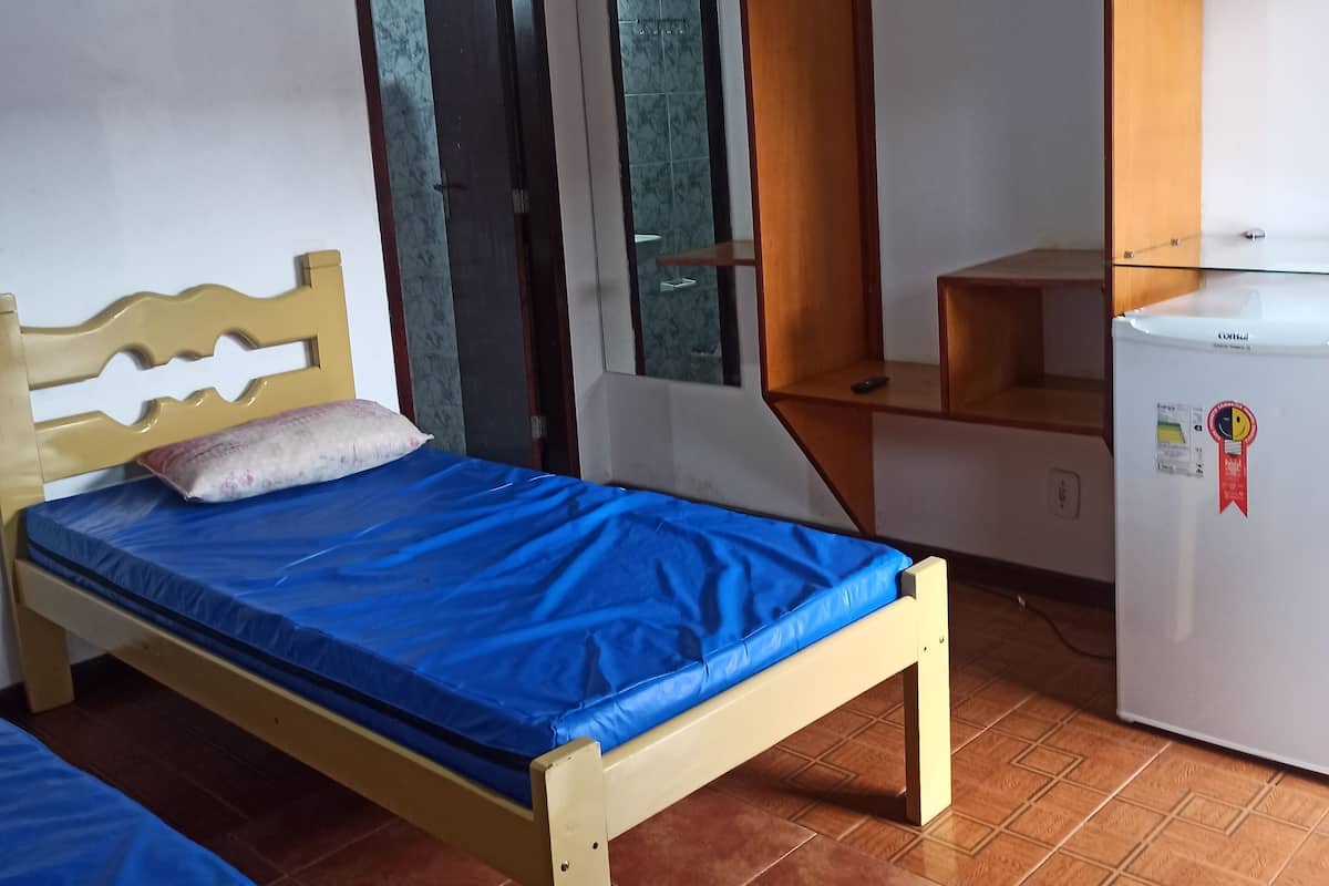 Une chambre avec un lit, un petit bureau, un miroir et un réfrigérateur.