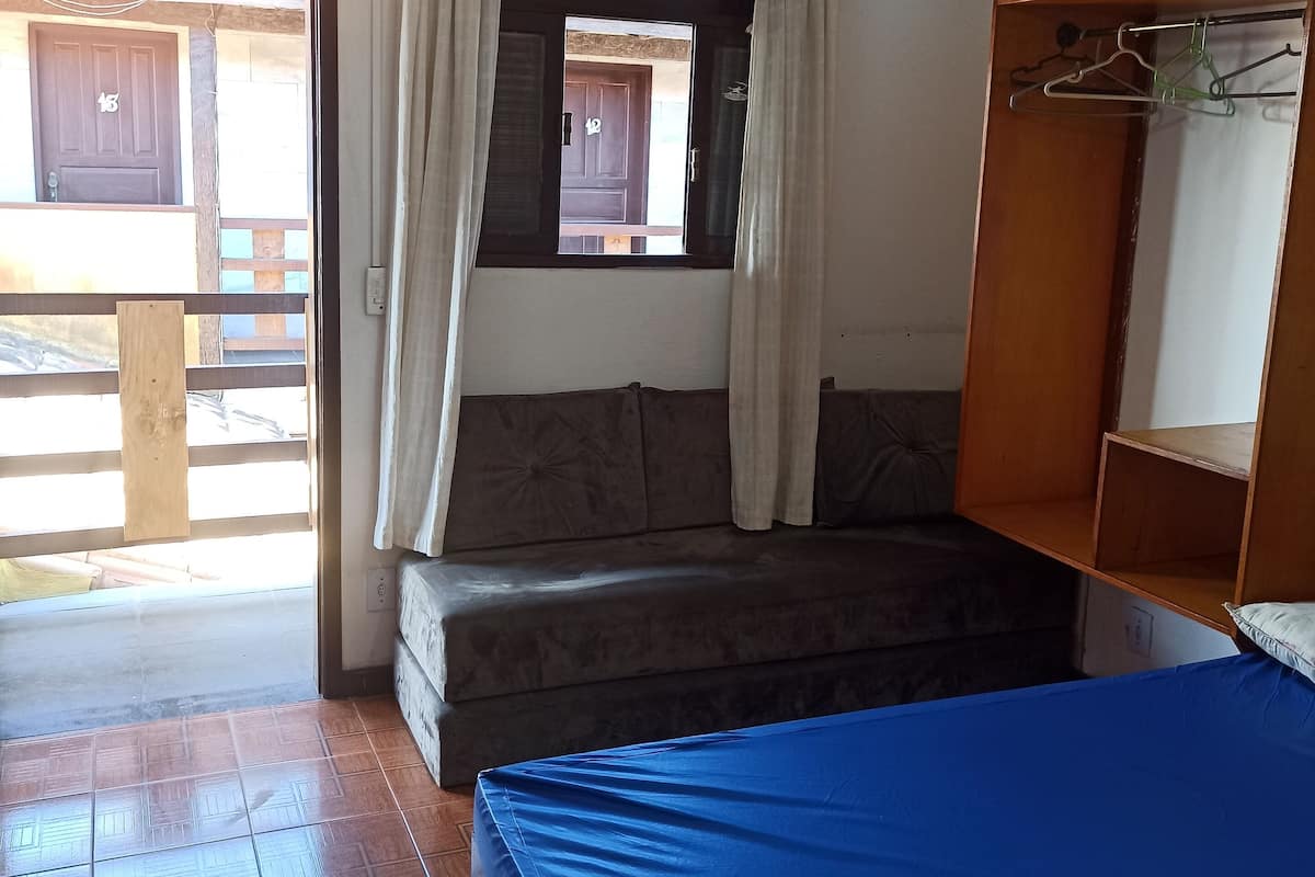Une pièce comprenant un lit, un banc en bois, une fenêtre avec des rideaux et un ventilateur de plafond.