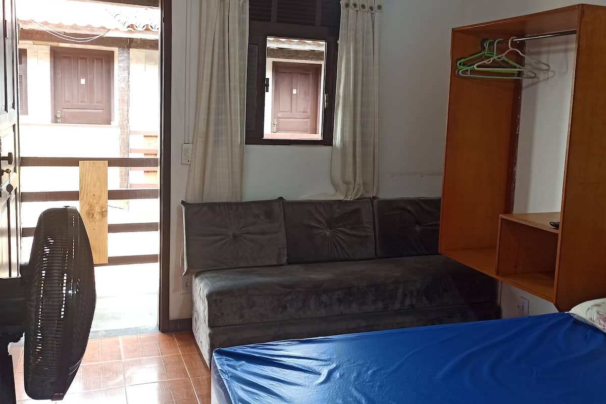 Une chambre avec un lit, un ventilateur, une fenêtre avec des rideaux, un ventilateur de plafond et une armoire en bois.