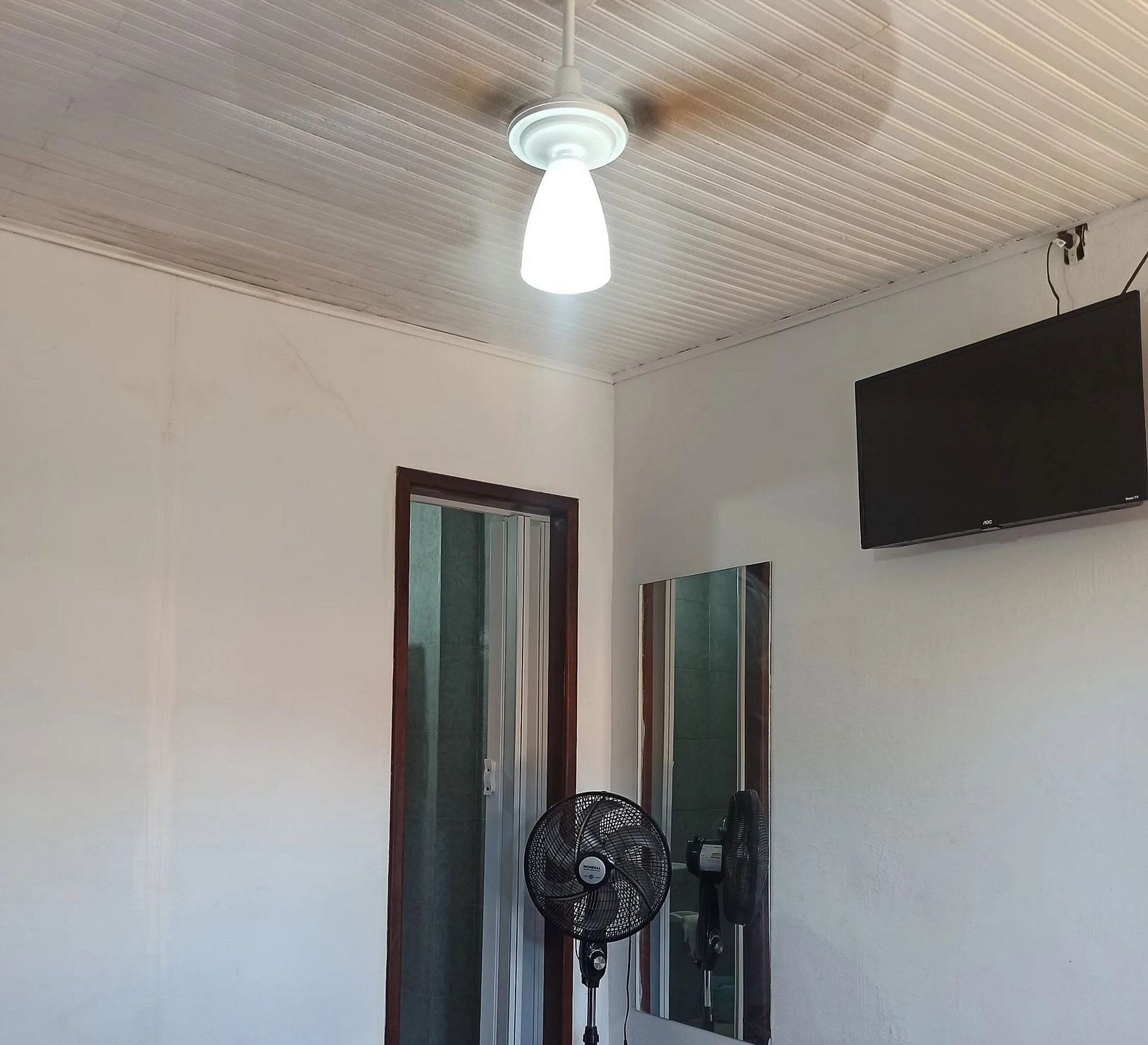 Une pièce dotée d’un ventilateur de plafond, d’un téléviseur fixé au mur et d’une porte avec un miroir.
