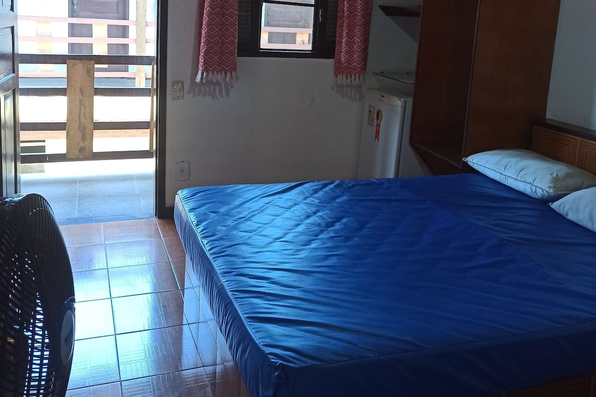 Une chambre avec un lit, une armoire, une fenêtre avec des rideaux et un ventilateur.