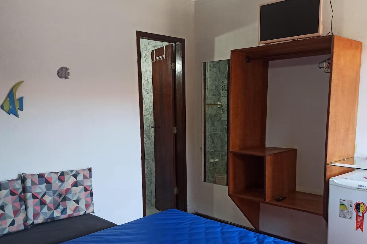 Une chambre avec un lit, un ventilateur de plafond, une armoire et un petit réfrigérateur.