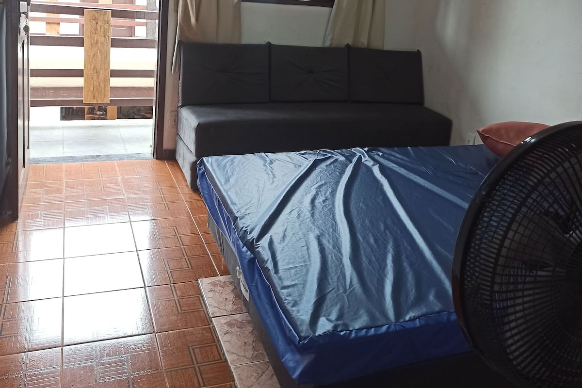 Une chambre à coucher avec un lit, un ventilateur de plafond, une fenêtre et une vue sur l’extérieur.
