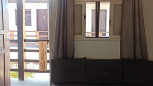 A room with a bed, a sofa, a window with curtains, and a view of the outside. - Buzios Geriba Aluguel Economico (Búzios)