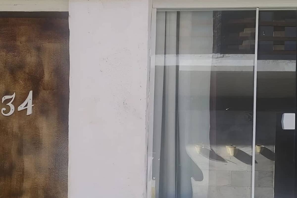 Une entrée d’immeuble avec une porte portant le numéro « 34 » et une porte vitrée dans laquelle on peut voir le reflet d’une personne.