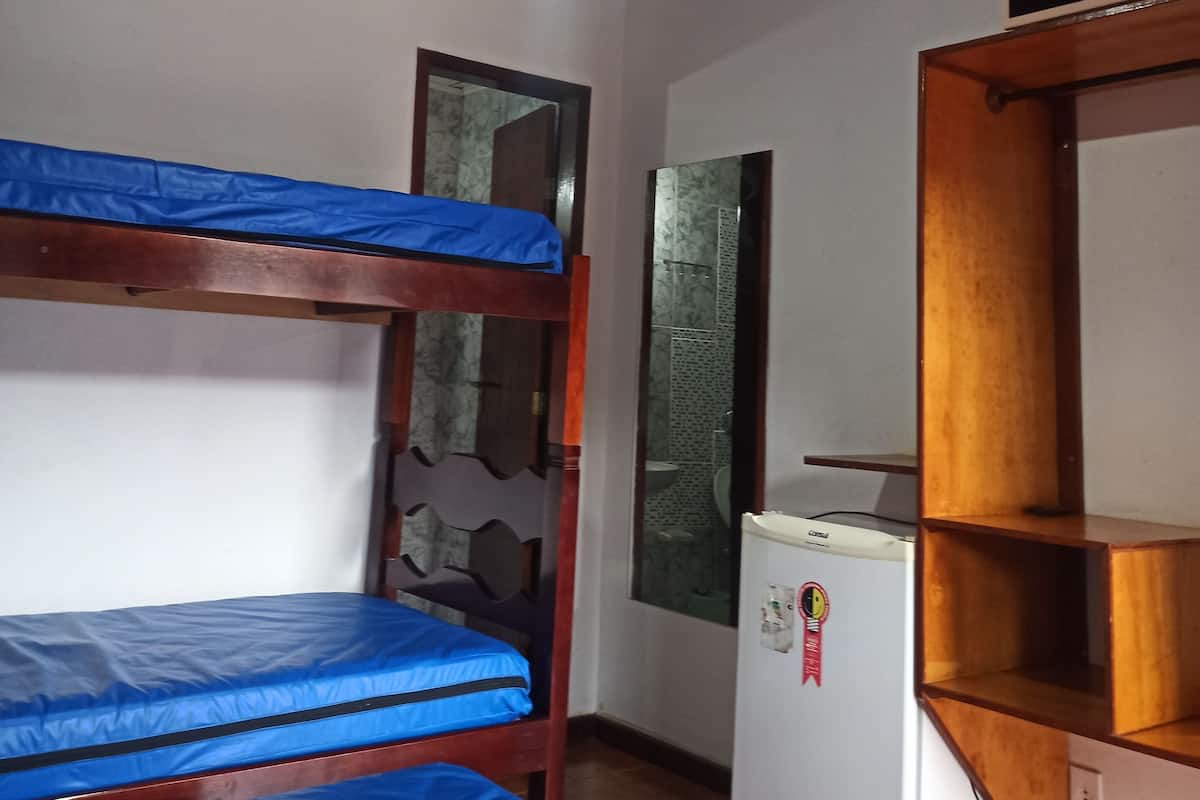 Une chambre avec des lits superposés, un ventilateur de plafond, un réfrigérateur et une étagère en bois.