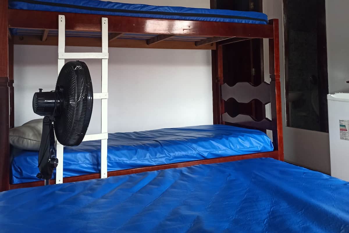 Une chambre avec un lit superposé, un ventilateur de plafond, une fenêtre et une porte.