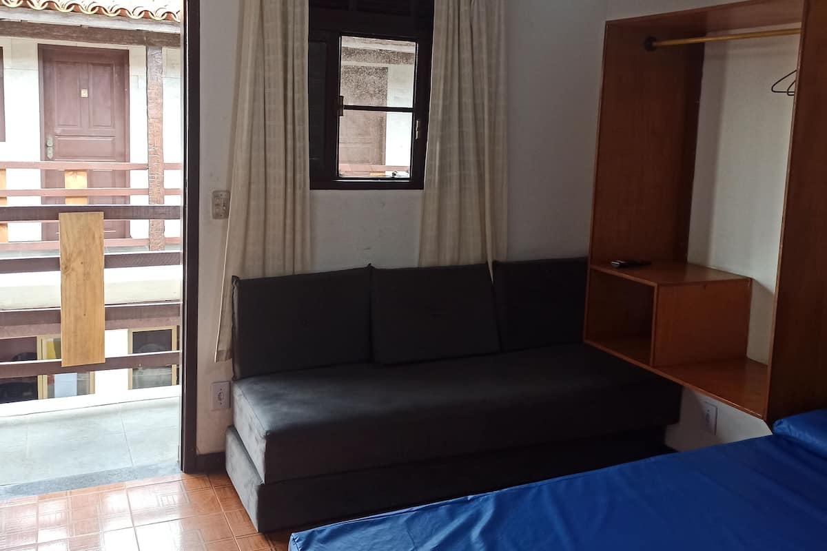Une pièce comprenant un lit, un canapé, un ventilateur de plafond, une fenêtre avec des rideaux et une porte en bois.