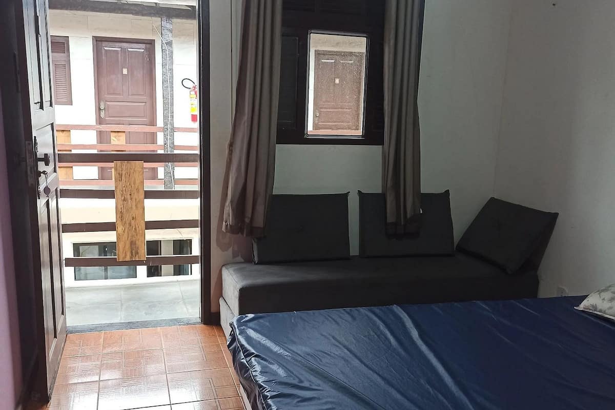 Une chambre à coucher avec un lit, une fenêtre avec des rideaux, une porte et une vue sur le balcon extérieur.