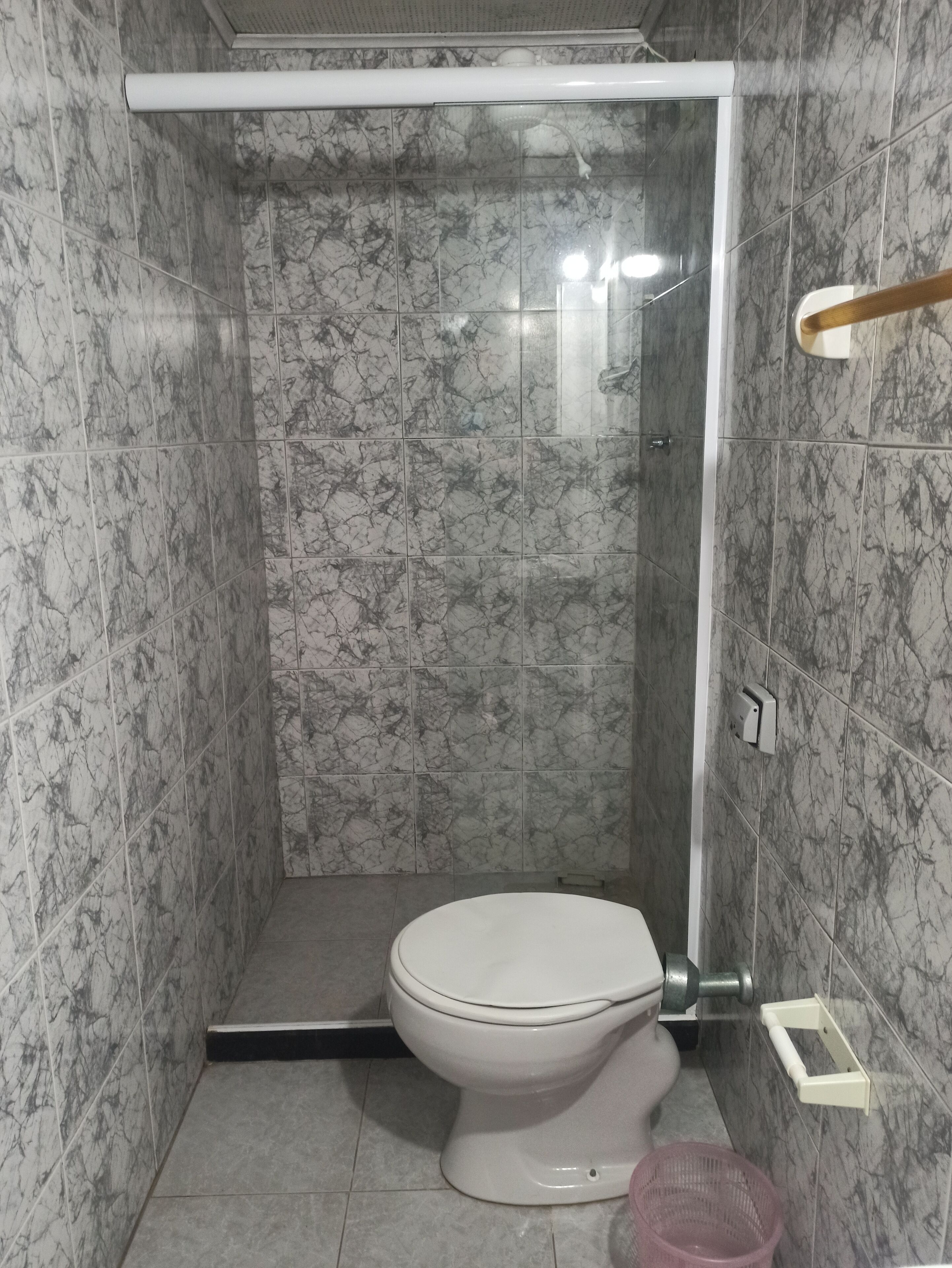 Um banheiro com vaso sanitário, chuveiro e paredes de mármore.