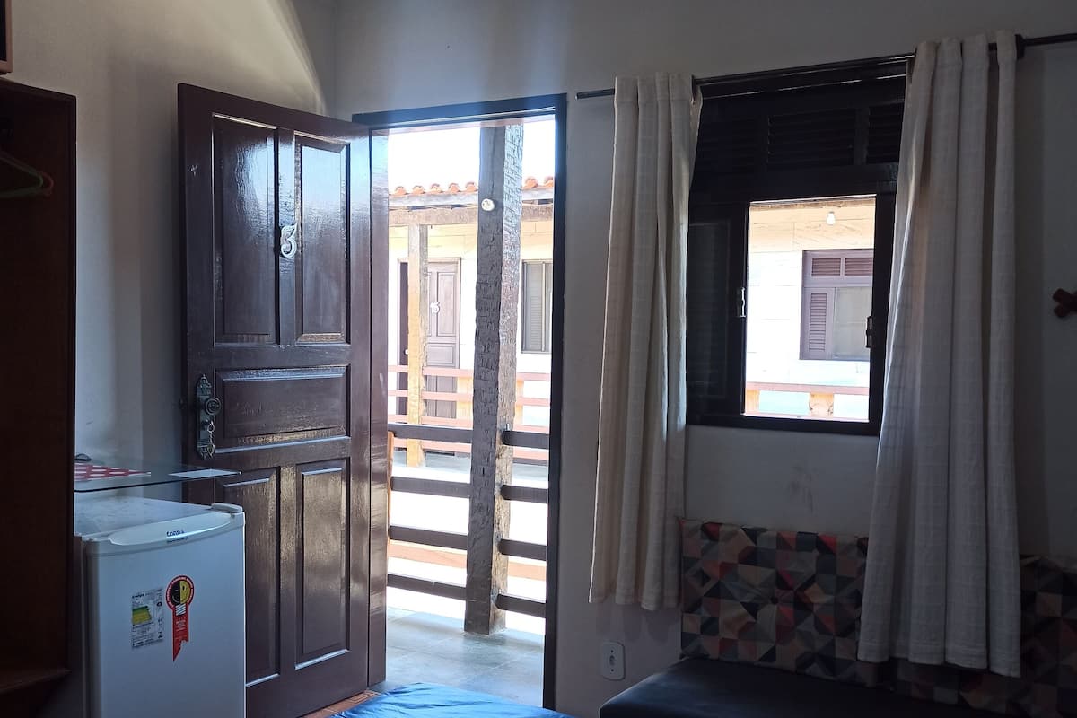 Une chambre comprenant un lit, un réfrigérateur, une porte donnant sur un espace extérieur et une fenêtre avec des rideaux.