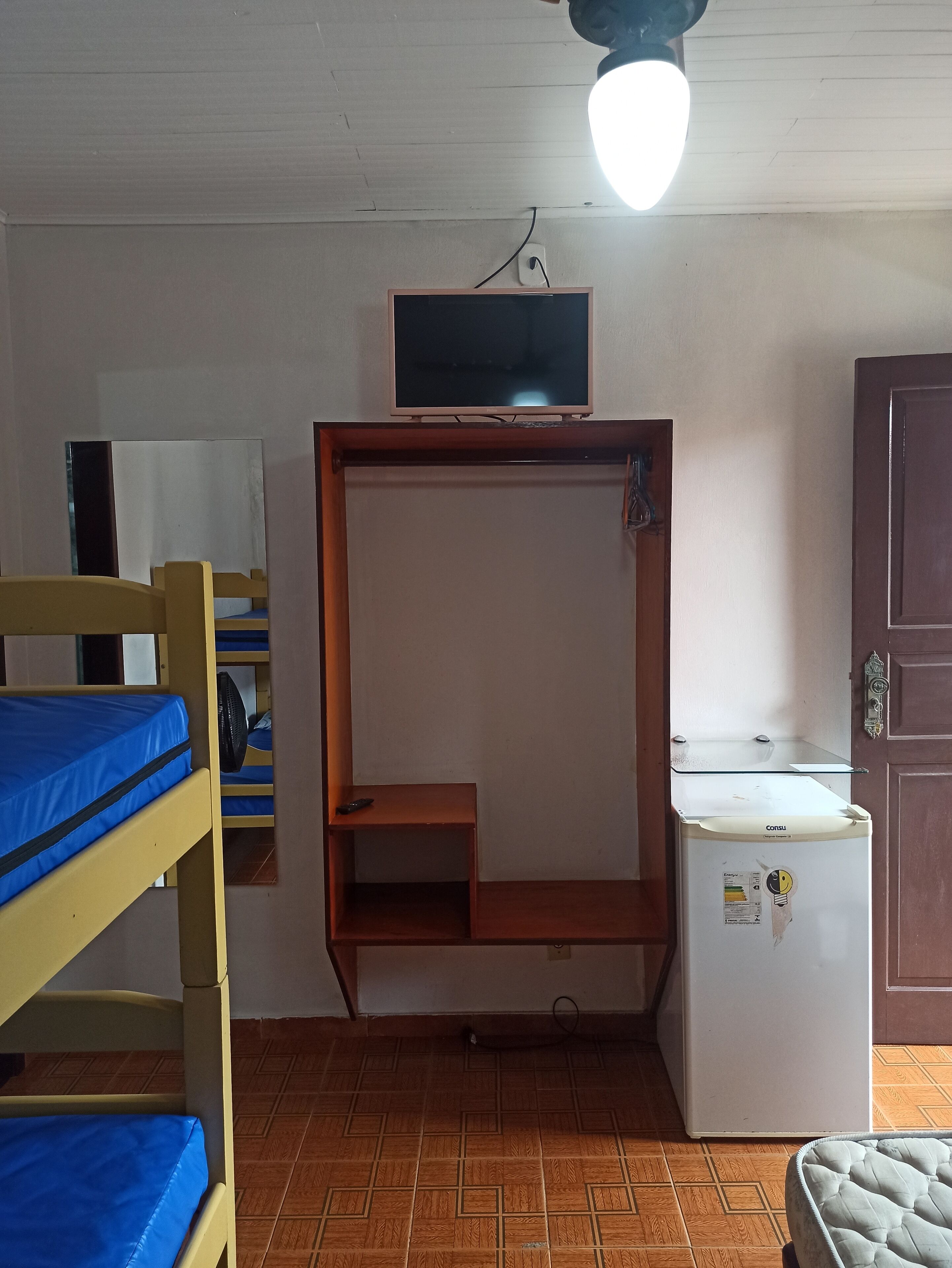 A dormitory room with bunk beds, a small desk, a television, and a refrigerator.