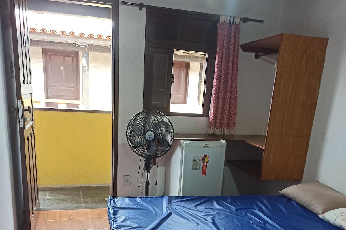 Une chambre avec un lit, un ventilateur, un réfrigérateur et une vue sur l’extérieur.