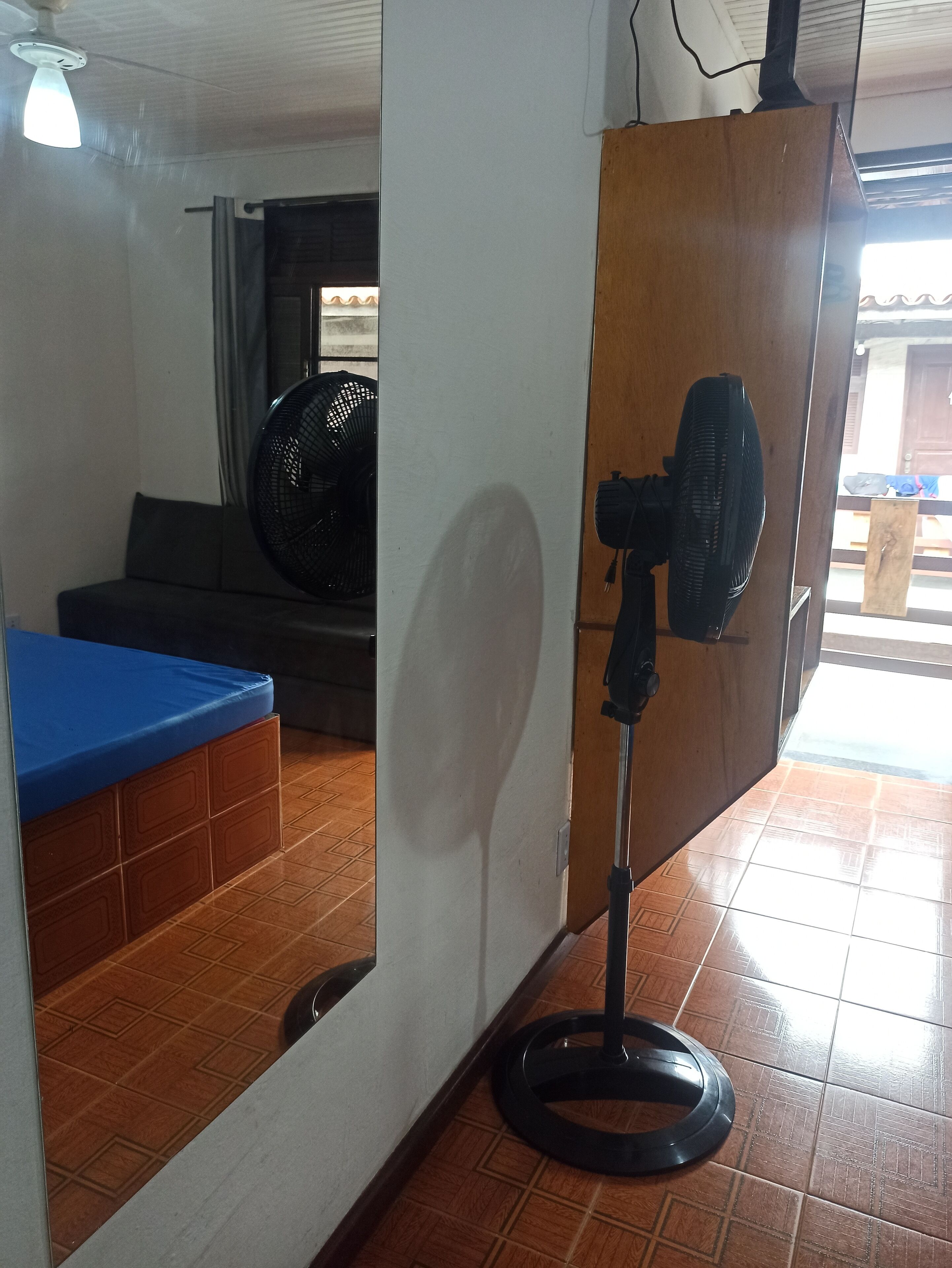 A room with a blue cushioned bench, a standing fan, and a tiled floor.