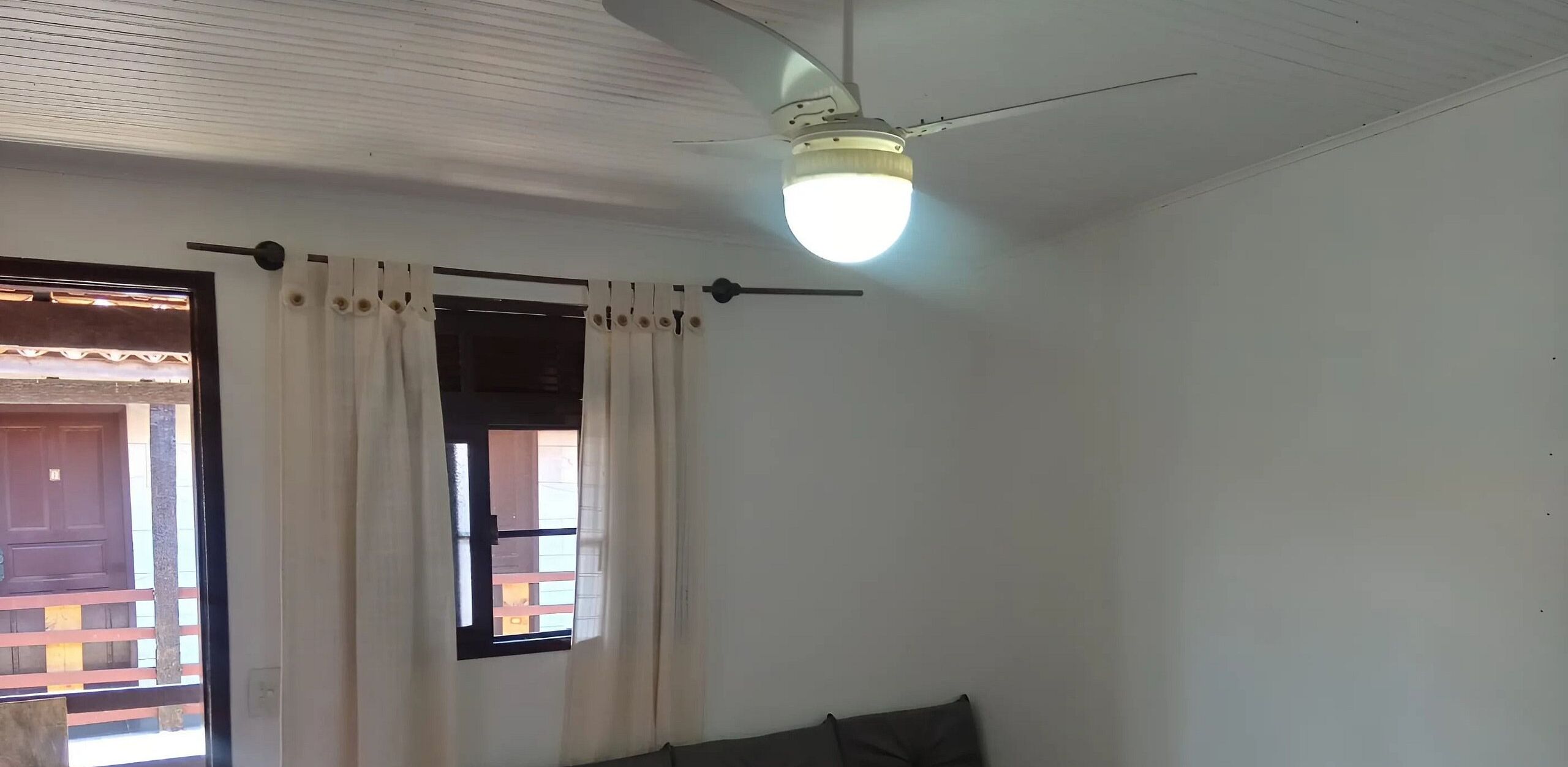 Una habitación con ventilador de techo, ventana con cortinas y vistas al exterior.