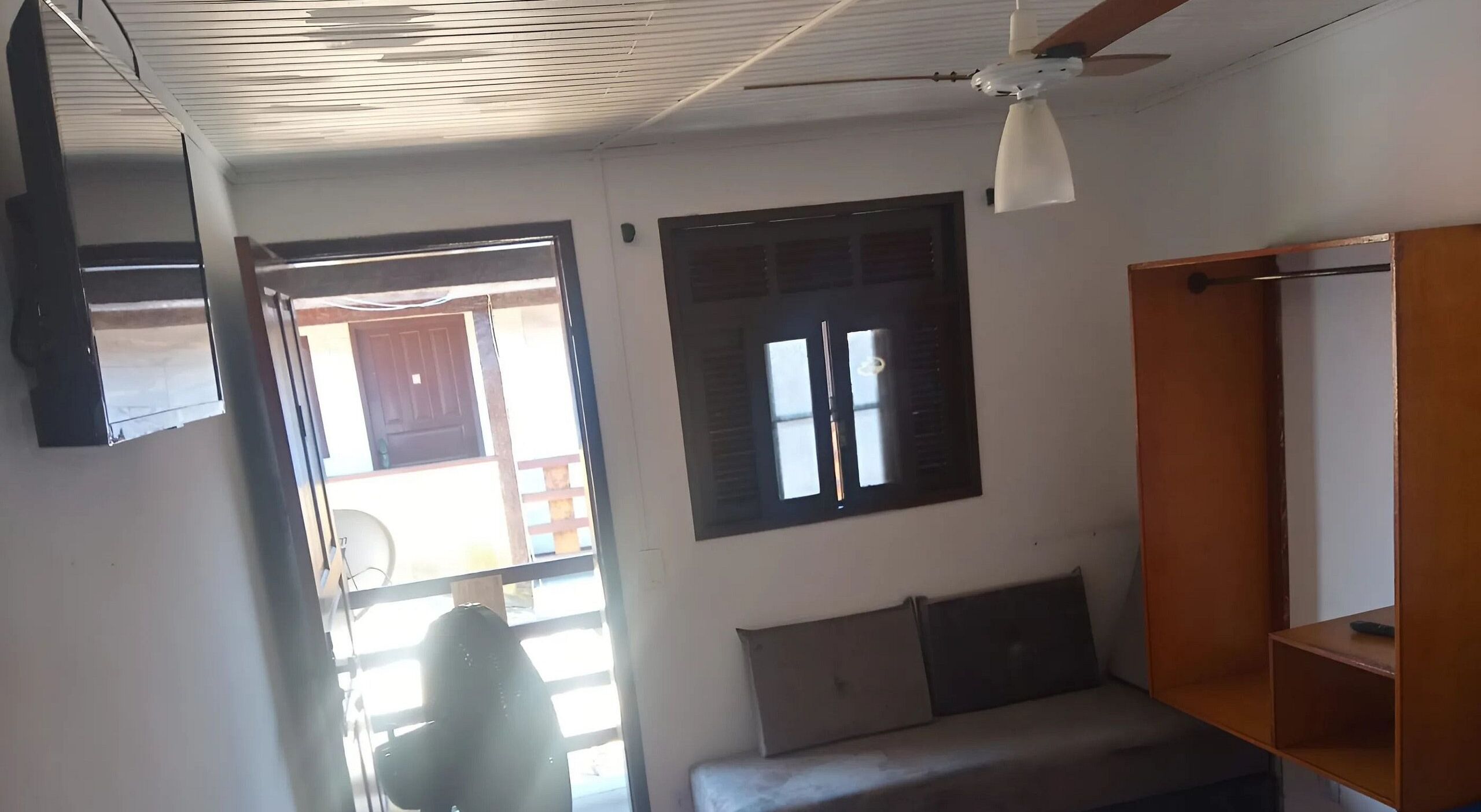 Ein Zimmer mit Deckenventilator, einem Fenster mit Rollläden, einer Couch und einem Holzregal.