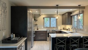 A modern kitchen with dark cabinets, a large island, and a view of the outdoors through a window. -  Walk To Town, Ski In Style - Stunning Views w/Hot Tub, 1 block to Free Shuttle (Breckenridge)