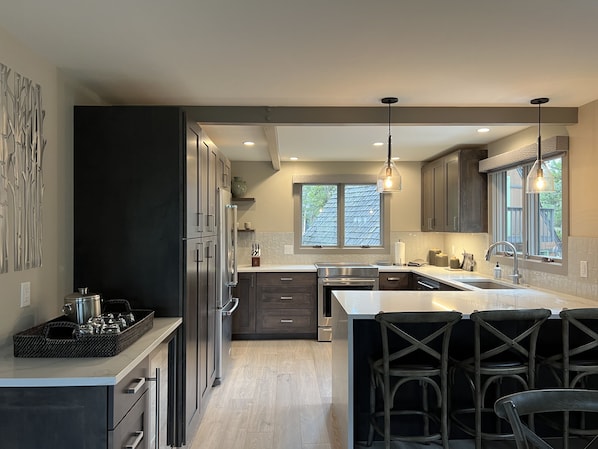 A modern kitchen with dark cabinets, a large island, and a view of the outdoors through a window.