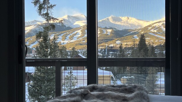 A room with a large window offering a view of snow-covered mountains and a ski resort. -  Walk To Town, Ski In Style - Stunning Views w/Hot Tub, 1 block to Free Shuttle (Breckenridge)