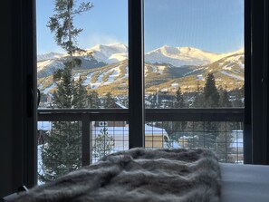 A room with a large window offering a view of snow-covered mountains and a ski resort.