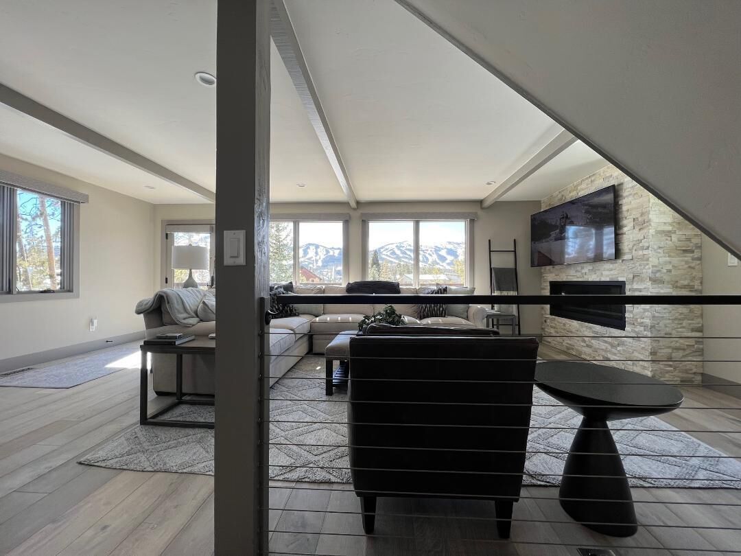 A spacious living room with a large window, a fireplace, and a flat-screen TV mounted on the wall.
