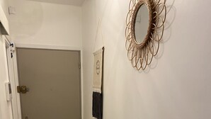 Ein Flur mit einer geschlossenen Tür, einem Wandspiegel und einer Wanddekoration aus Makramee.