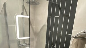 Ein moderner Duschbereich mit Glastür, Handbrause und einem an der Wand befestigten Handtuchhalter.