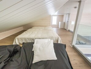 A room with a sloped ceiling, a bed with a white duvet and pillows, and a window providing natural light.