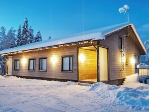 Una cabaña de madera con techo nevado, una entrada visible y un pequeño porche.