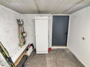 Una habitación pequeña y sencilla con una puerta blanca, un armario blanco y una estantería con esquíes y bastones de esquí.