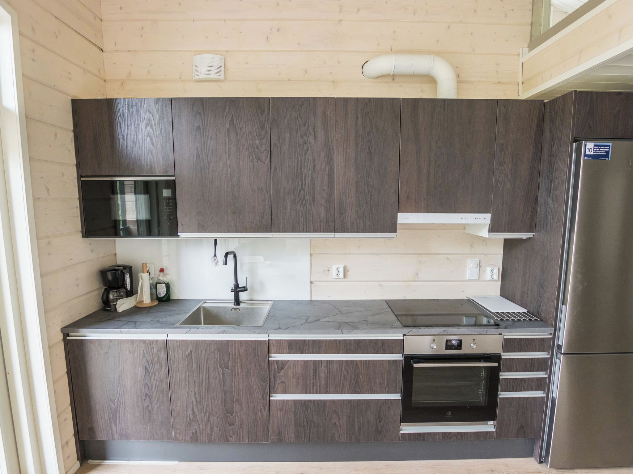 A modern kitchen with dark wood cabinets, a stainless steel refrigerator, a built-in oven, and a microwave.