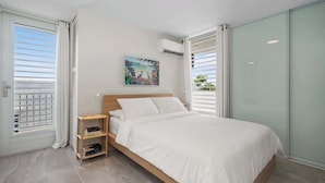 A bedroom with a bed, a nightstand, a painting, and a window with blinds. - Beautiful Queen Penthouse with Large Terrace (San Juan)