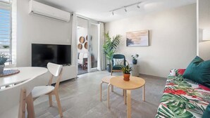 A modern living room with a flat-screen TV, a sofa with a tropical print, a dining area with a table and chairs, and a sliding glass door leading to another room. - Beautiful Queen Penthouse with Large Terrace (San Juan)