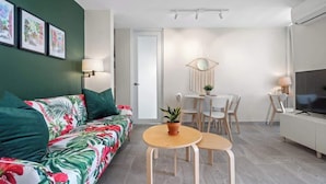 A modern living room with a sofa, two small tables, a TV, and a dining area with chairs and a table. - Beautiful Queen Penthouse with Large Terrace (San Juan)