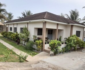 Ein zweistöckiges Haus mit flachem Dach, einer Veranda und einem Garten mit verschiedenen Pflanzen.