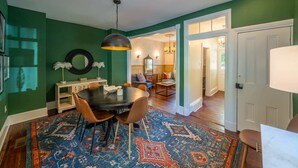 A dining area with a round table, chairs, and a patterned rug. There is a mirror on the wall and a hanging light fixture above the table. - Spacious 3BR Historic Home | Walk Downtown+Parking (Kennett Square)