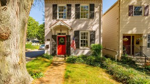 A two-story house with a red door, a front porch, and a small garden. - Spacious 3BR Historic Home | Walk Downtown+Parking (Kennett Square)