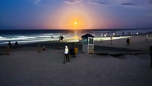 Una playa al atardecer con una torre de salvavidas, bañistas y un mar tranquilo.