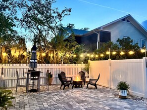 Un patio al aire libre con un brasero, asientos e iluminación con luces colgantes.