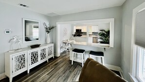 Una sala de estar moderna con comedor, muebles blancos y vista a la cocina.