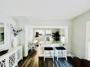 A modern kitchen with white cabinetry, a dining area with a white table and chairs, and a bar area with stools.