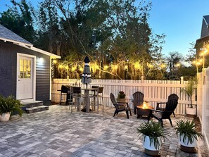 A patio area with a fire pit, outdoor furniture, and string lights.