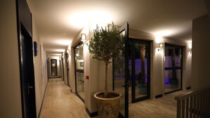 A hotel hallway with a potted tree, glass doors, and wall-mounted lights. - Ariel Hotel Alaçatı (Cesme)