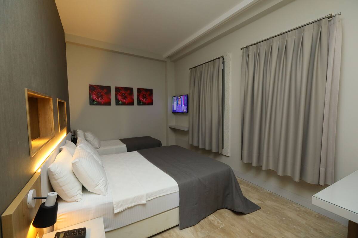A modern hotel room with a bed, bedside table, lamp, artwork, curtains, and a television.