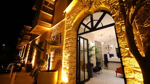 A hotel entrance with a stone facade, a large arched doorway, and a reception desk inside. - Ariel Hotel Alaçatı (Cesme)