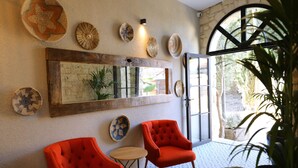 A room with two red armchairs, a small round table, and a large mirror on the wall. There are several woven baskets and a potted plant. - Ariel Hotel Alaçatı (Cesme)