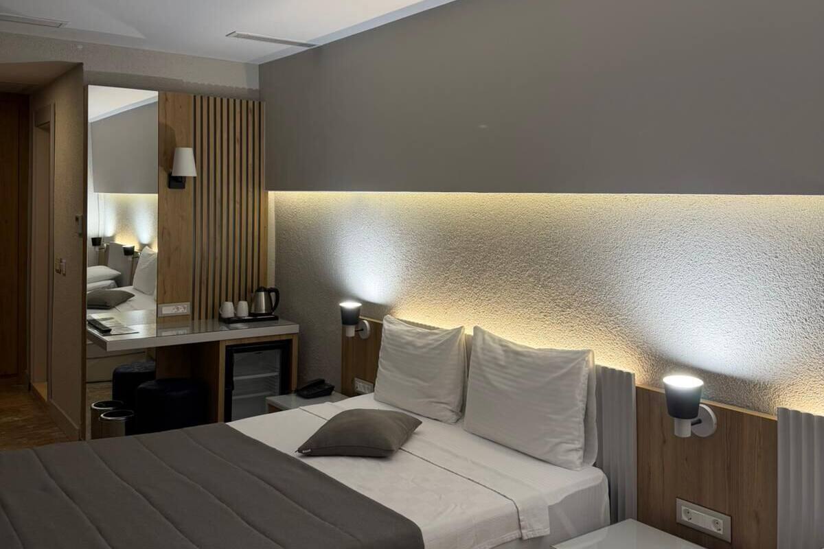A modern hotel room with a bed, bedside tables, a desk, and a mirror.
